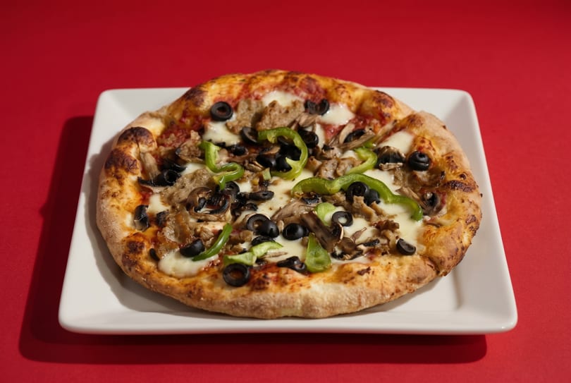 A whole pizza with green peppers, black olives, mushrooms, and sausage on a white plate.